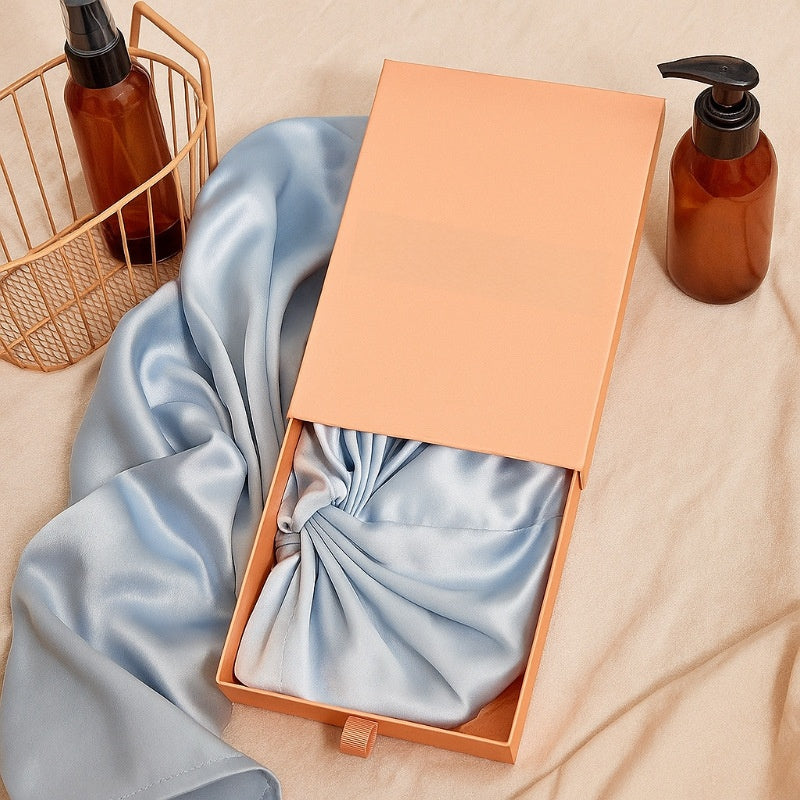 Open box with blue satin bow, beige basket, and brown bottles on a beige surface