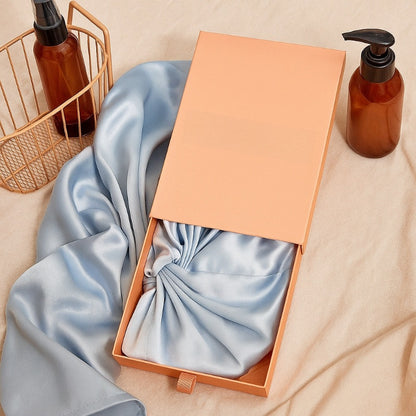 Open box with blue satin bow, beige basket, and brown bottles on a beige surface