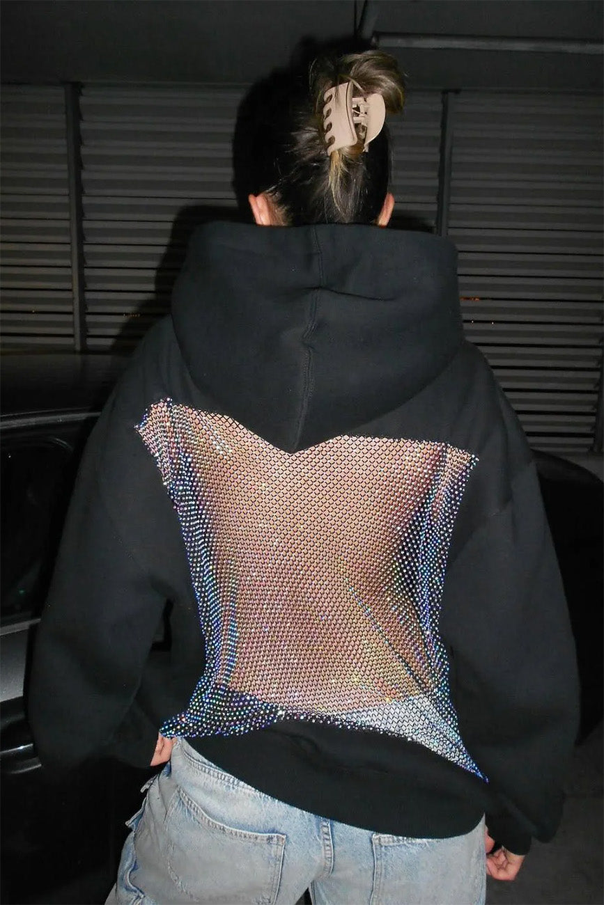 Person wearing a black hoodie with a colorful pattern on the back, standing in a dark room.