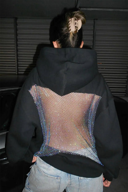 Person wearing a black hoodie with a colorful pattern on the back, standing in a dark room.