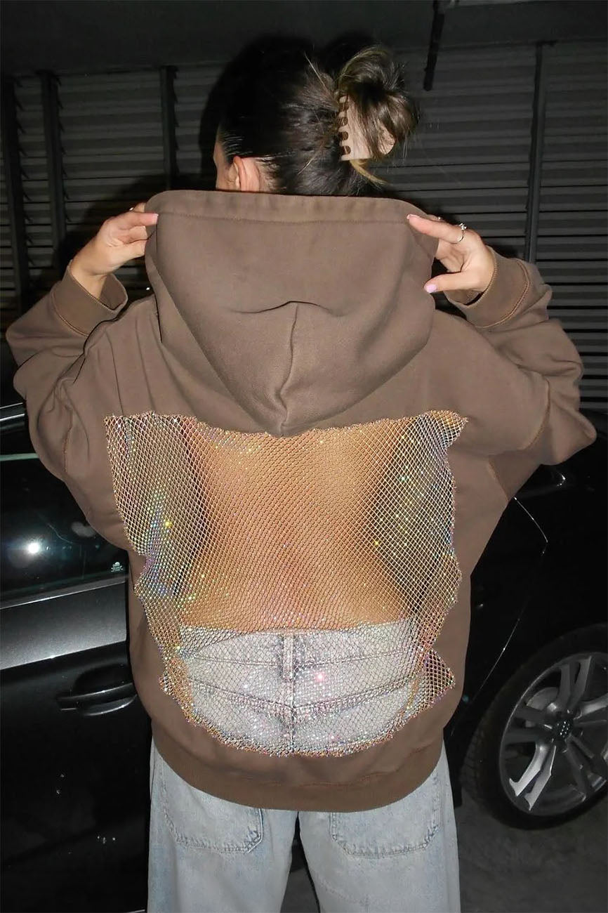 Person wearing a brown hoodie with a mesh back panel, standing in front of a car at night.