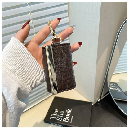 Hand holding a brown leather key case with a metallic finish, blurred background