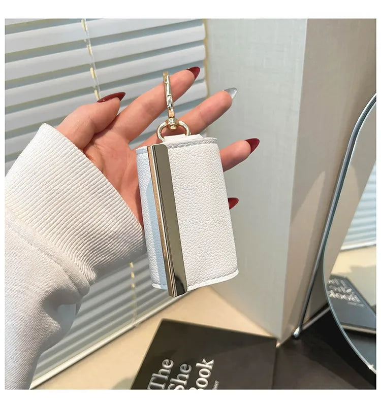 Hand holding a small white textured handbag with a gold chain in front of a mirror.