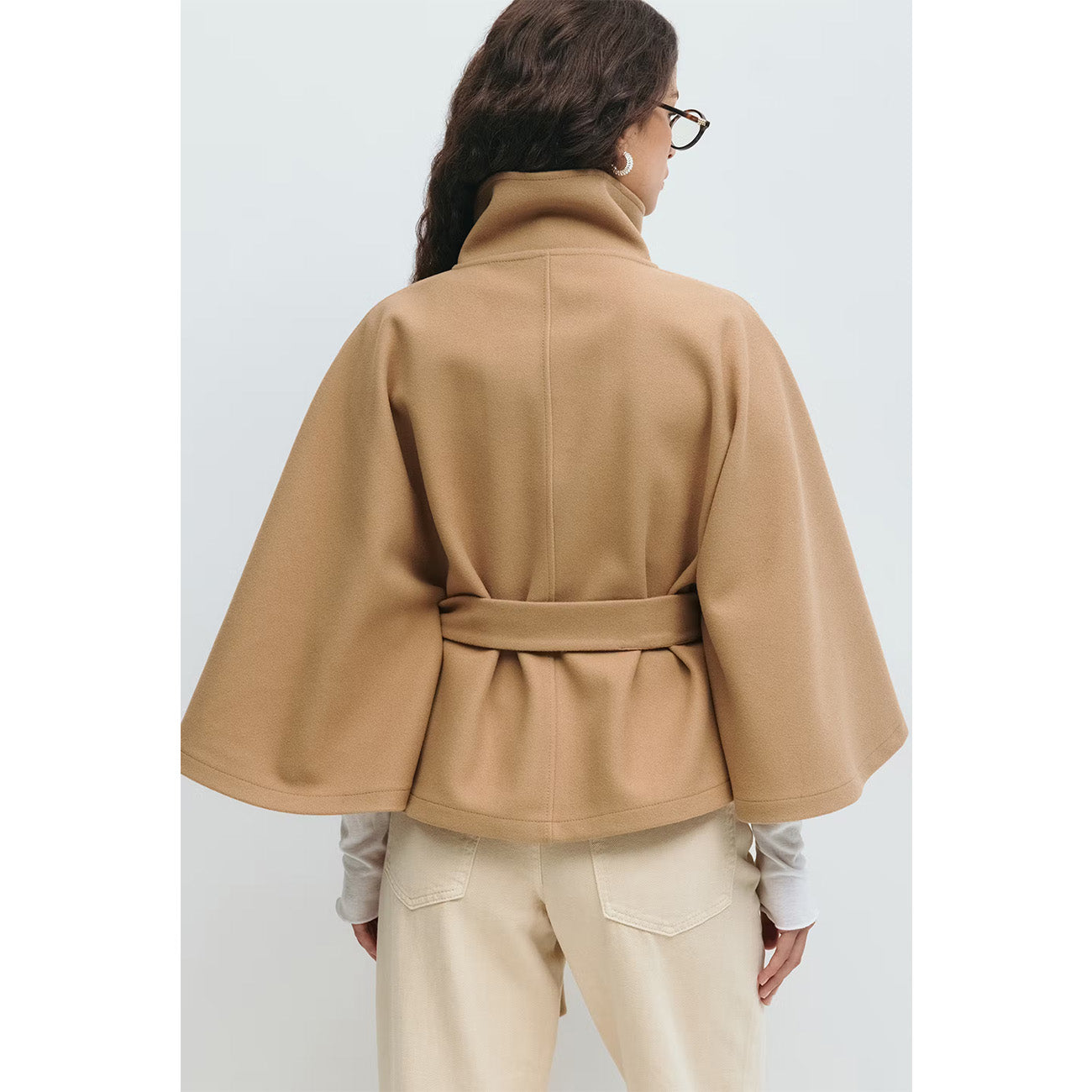 Person wearing a beige jacket with a belt on a white background