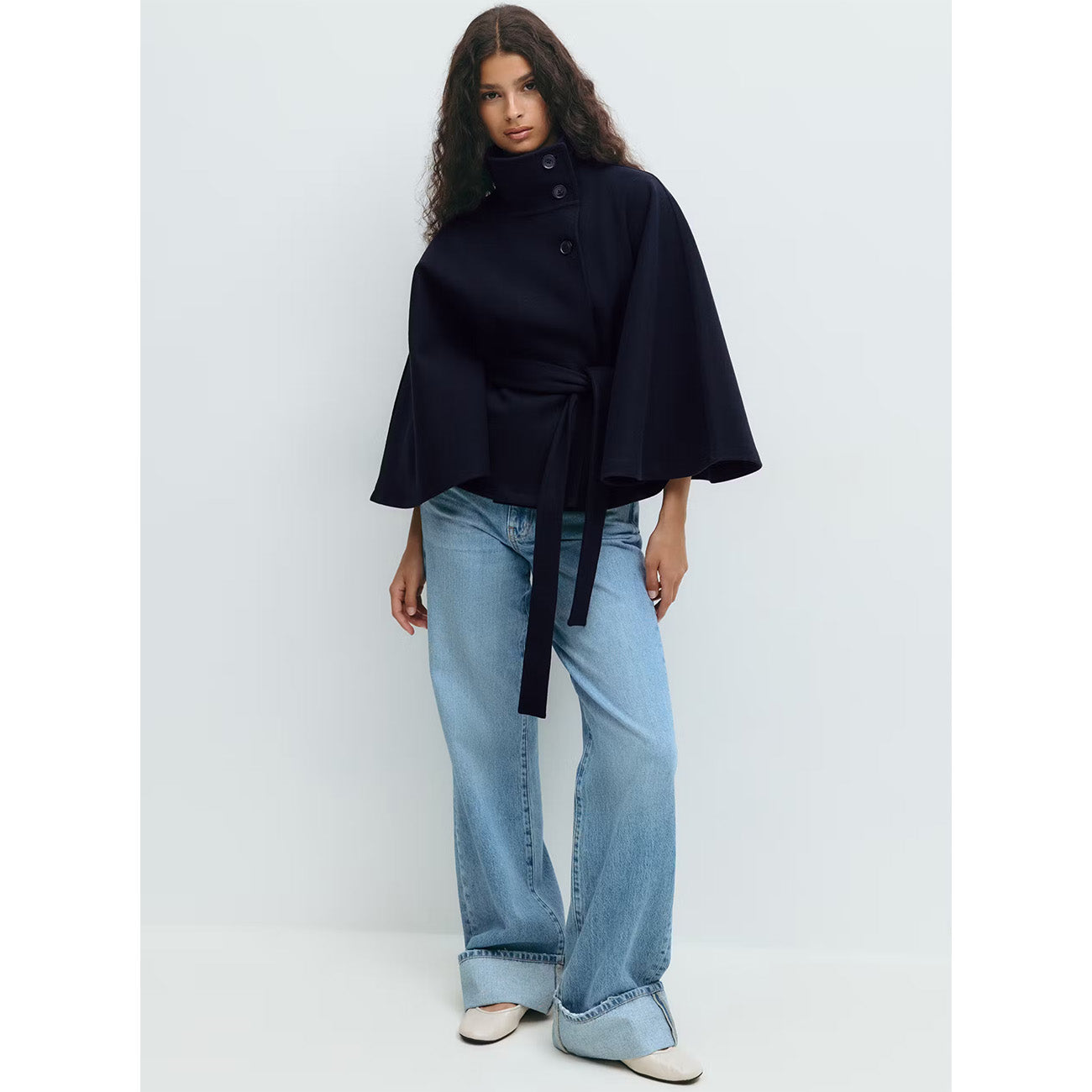 Woman wearing a black cape and light blue jeans on a white background