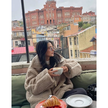 Woman sitting on a balcony with a cup of coffee and a pastry, with a cityscape in the background.