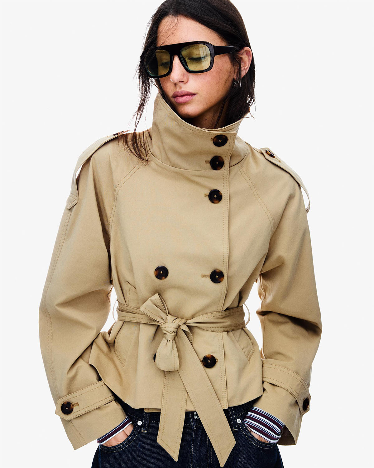 Person wearing a beige trench coat with black buttons on a white background